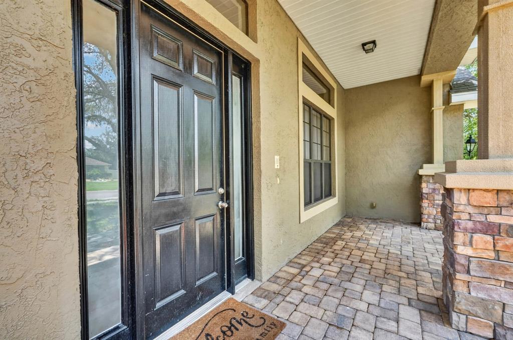 A front porch with a black door, sidelights, and stone-accented columns over paver flooring — 1517 CLAPTON DRIVE, DELAND, FL