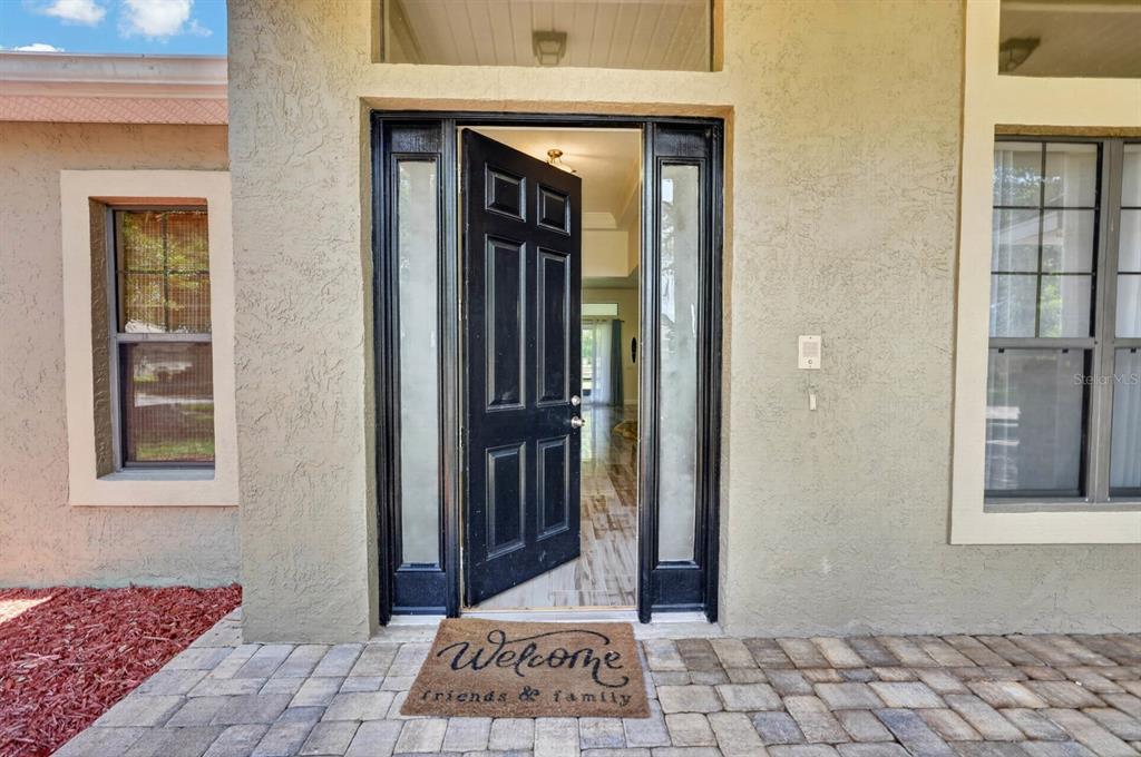 A front entrance with a black door, sidelights, and a welcome mat on a paved porch — 1517 CLAPTON DRIVE, DELAND, FL