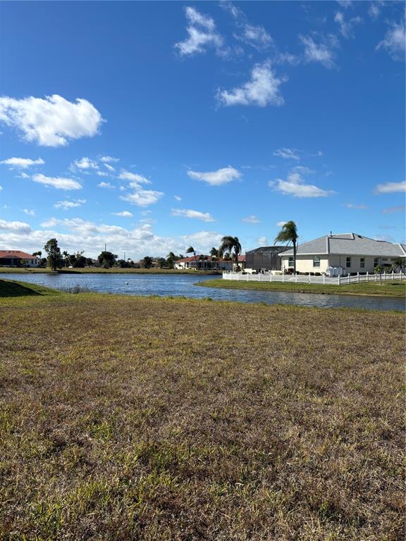 A grassy vacant lot overlooks a lake with houses in the background under a blue sky — 17283 CARROWAY LANE, PUNTA GORDA, FL