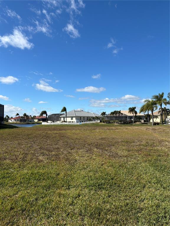 A vacant grassy lot overlooks a small lake and several houses under a blue sky — 17283 CARROWAY LANE, PUNTA GORDA, FL