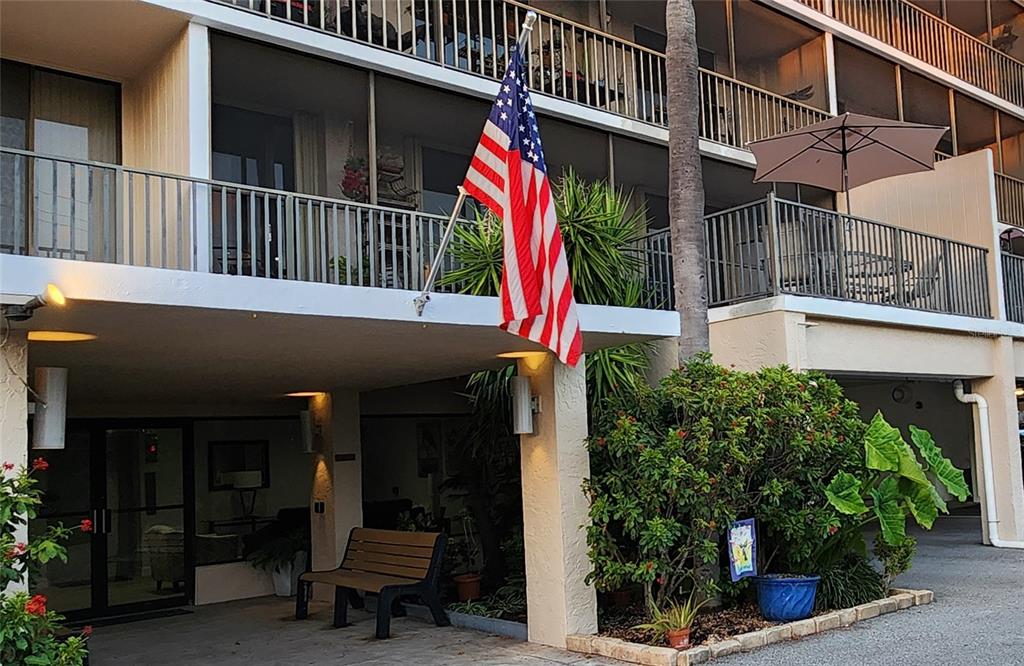 An American flag hangs from the balcony of a multi-story apartment building with landscaping — 25188 MARION AVENUE UNIT D104, PUNTA GORDA, FL
