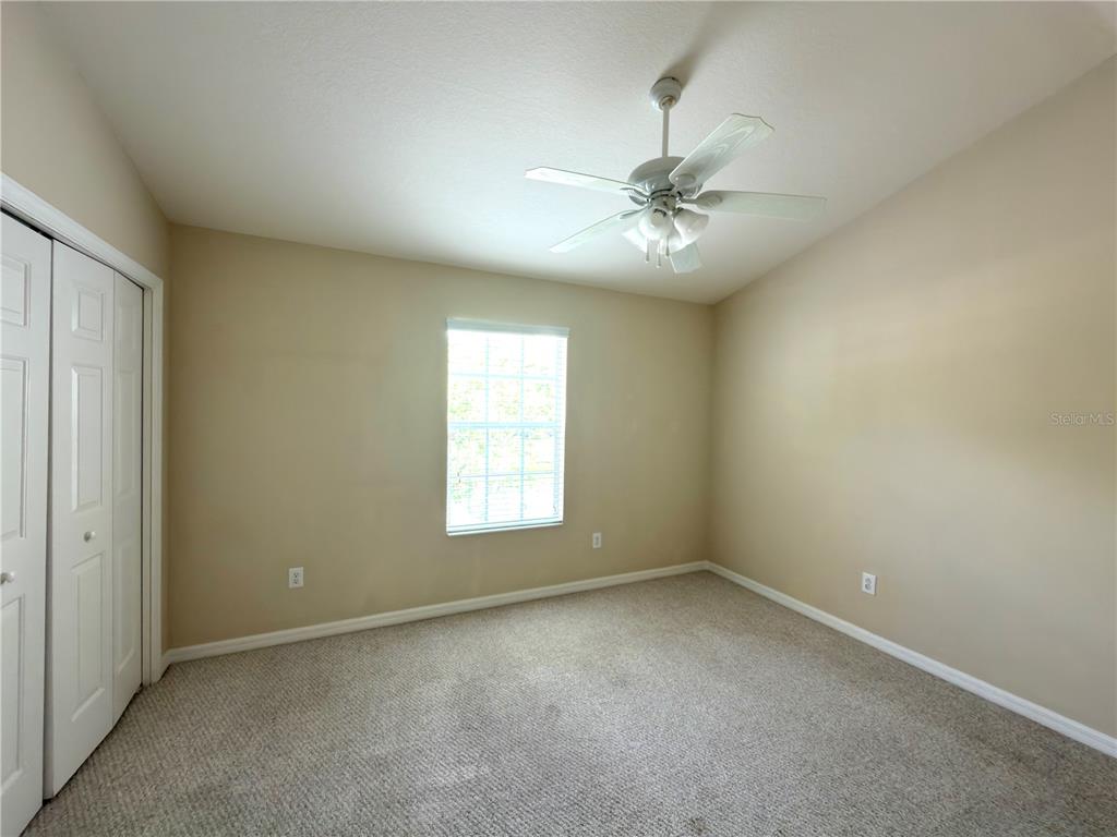 An empty bedroom features beige walls, carpeted flooring, a ceiling fan, and a window — 2437 EARLSWOOD COURT, BRANDON, FL