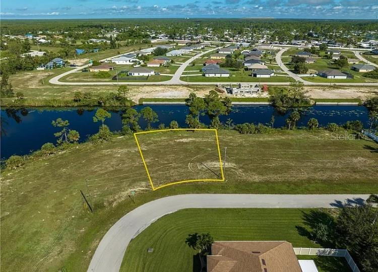 An aerial view shows a vacant, yellow-outlined residential lot situated along a canal — 2117 NE 43RD LANE, CAPE CORAL, FL