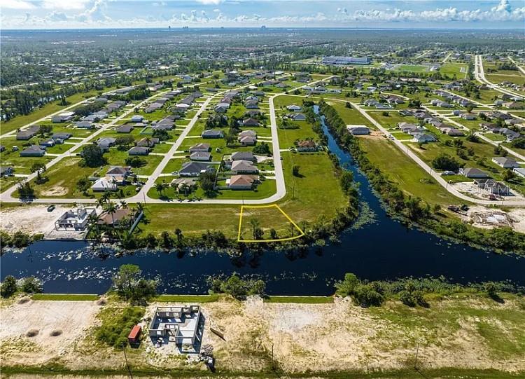An aerial view shows a vacant residential lot outlined in yellow next to a canal — 2117 NE 43RD LANE, CAPE CORAL, FL