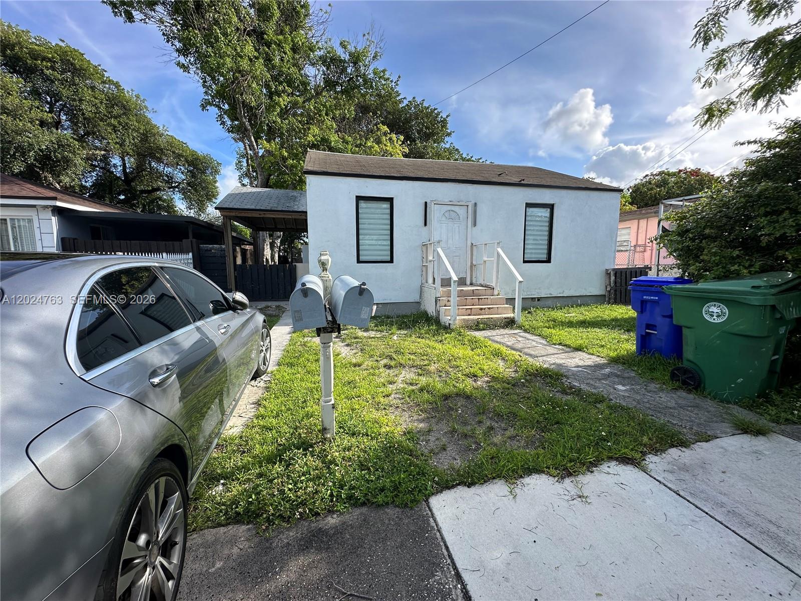 A small, white, single-story house features a front porch, a driveway, and two trash bins — 1773 NW 45th St, Miami FL 33142, MIAMI, FL