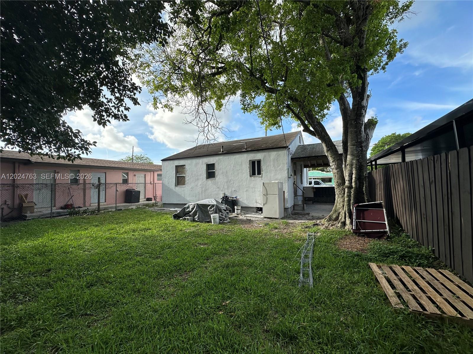 A backyard view shows a white house with a large tree and a wooden fence — 1773 NW 45th St, Miami FL 33142, MIAMI, FL