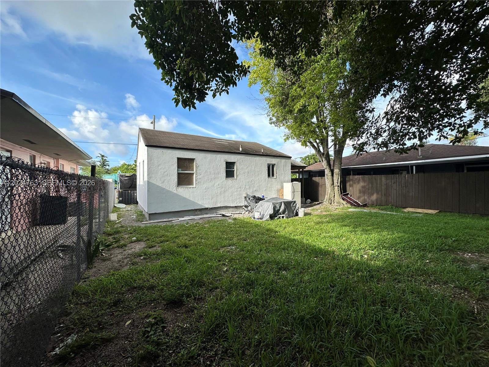 A white stucco house sits in a grassy backyard enclosed by a chain-link fence — 1773 NW 45th St, Miami FL 33142, MIAMI, FL