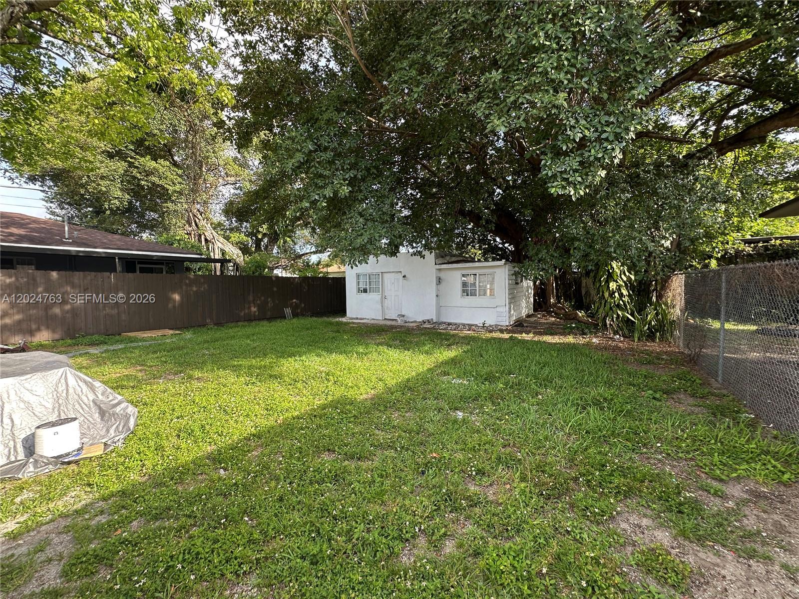 A small white detached structure sits in a grassy backyard shaded by a large tree — 1773 NW 45th St, Miami FL 33142, MIAMI, FL