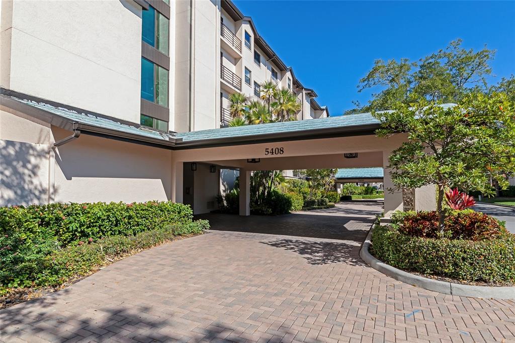 A paved driveway leads to a covered entrance of a multi-story building with landscaping — 5408 EAGLES POINT CIRCLE UNIT 302, SARASOTA, FL
