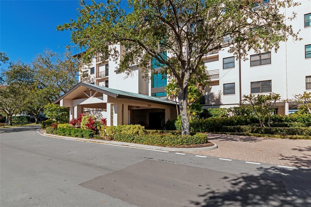 A multi-story apartment building features a covered entrance with a paved driveway and landscaping — 5408 EAGLES POINT CIRCLE UNIT 302, SARASOTA, FL