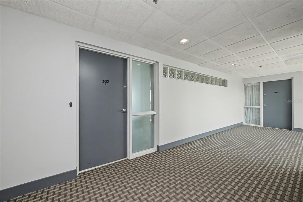 A hallway features gray doors numbered 302 and 303, patterned carpet, and glass block accents — 5408 EAGLES POINT CIRCLE UNIT 302, SARASOTA, FL