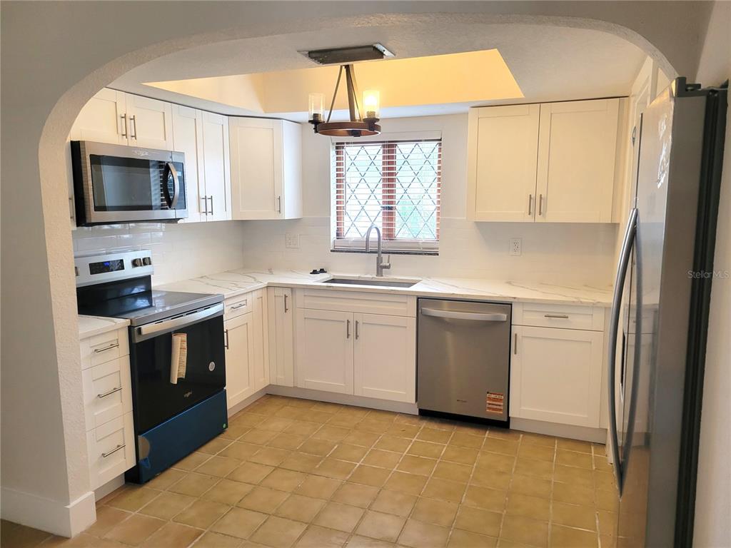 A kitchen features white cabinets, stainless steel appliances, marble-look countertops, and a tiled floor — 1835 MARYLAND AVENUE NE, ST PETERSBURG, FL