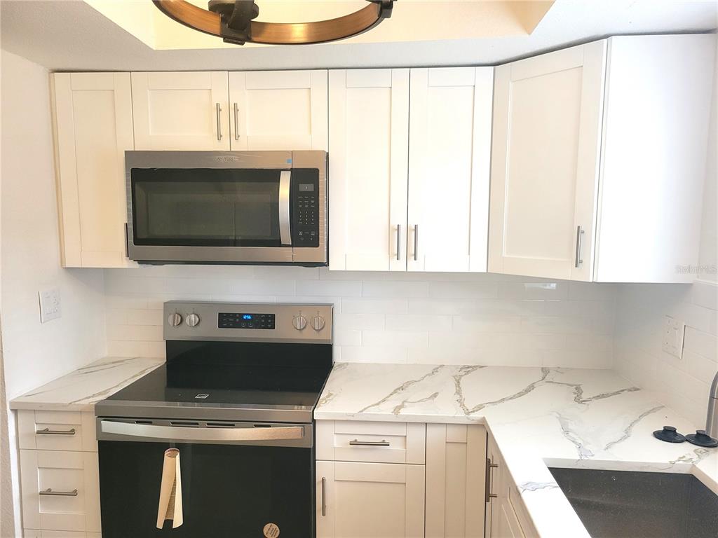 A kitchen features white shaker cabinets, marble-look countertops, a stainless steel microwave, and a stove — 1835 MARYLAND AVENUE NE, ST PETERSBURG, FL