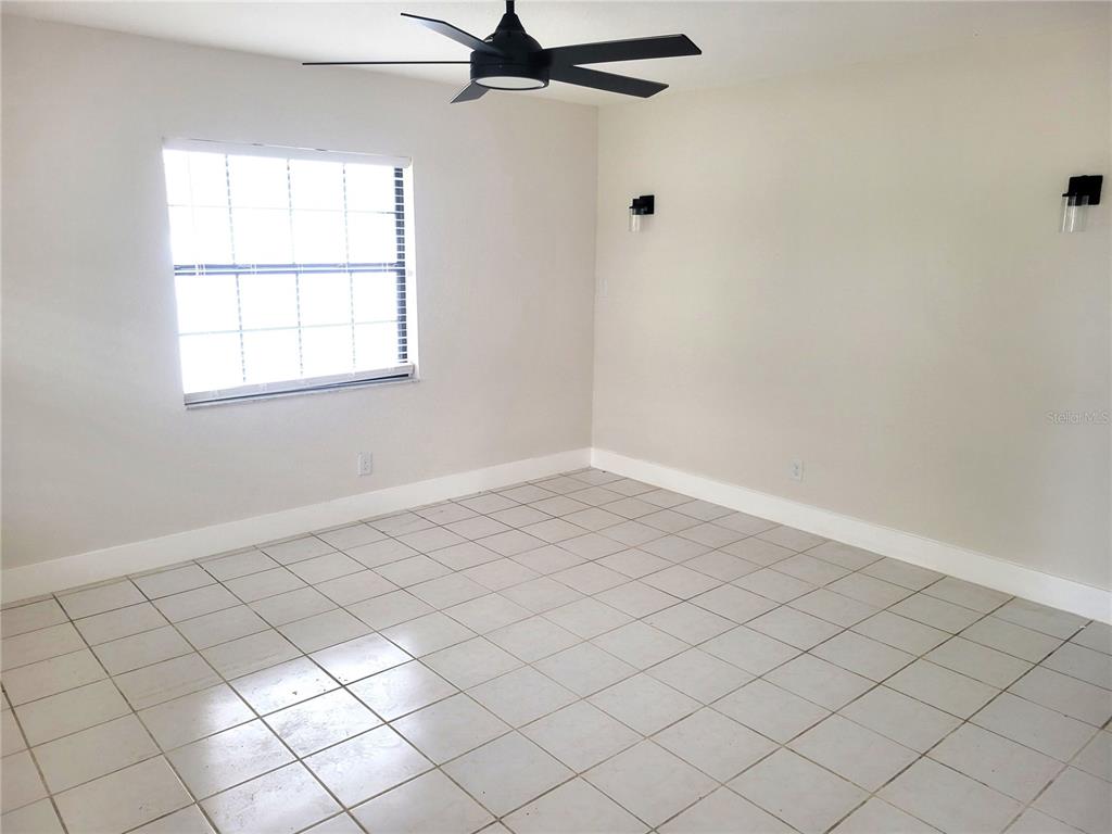 An empty room features light-colored tile flooring, a ceiling fan, and two wall-mounted light fixtures — 1835 MARYLAND AVENUE NE, ST PETERSBURG, FL