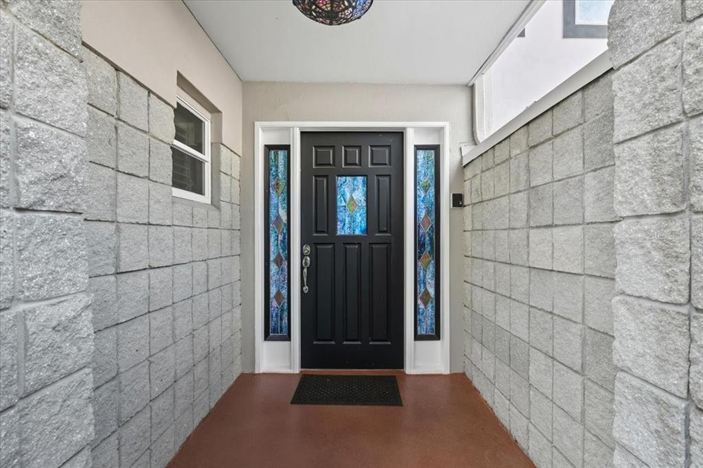 A black front door with stained glass panels is flanked by gray concrete block walls — 2713 CHAMBRAY LANE, TAMPA, FL