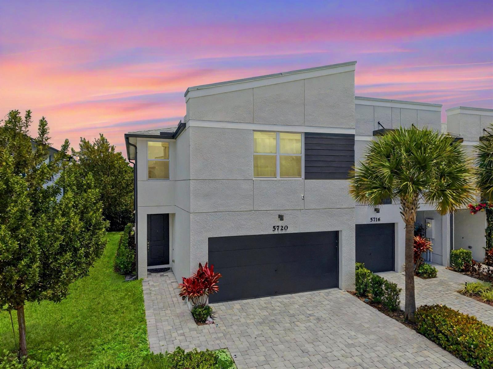A modern two-story townhouse with a gray garage and a paved driveway at sunset — 5720 Mentmore Drive, West Palm Beach FL 33407, WEST PALM BEACH, FL
