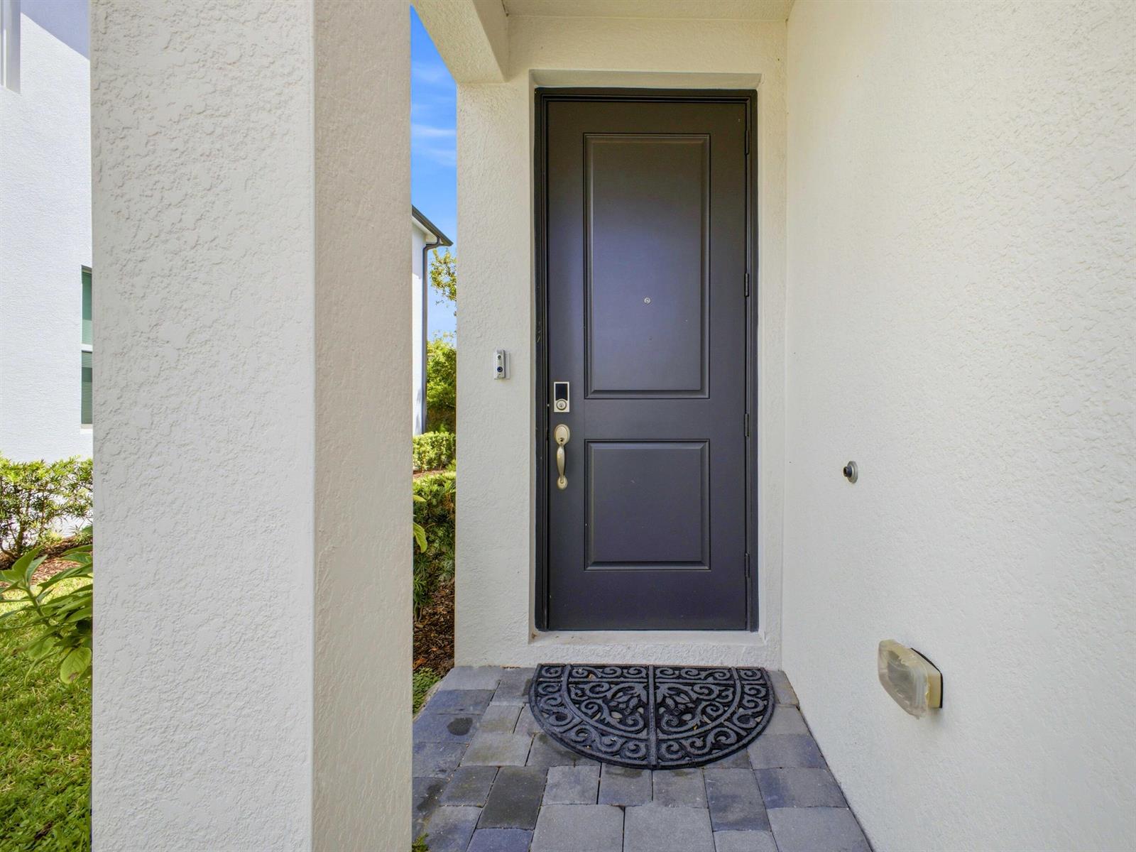 A dark gray front door is set within a white stucco entryway with stone pavers — 5720 Mentmore Drive, West Palm Beach FL 33407, WEST PALM BEACH, FL