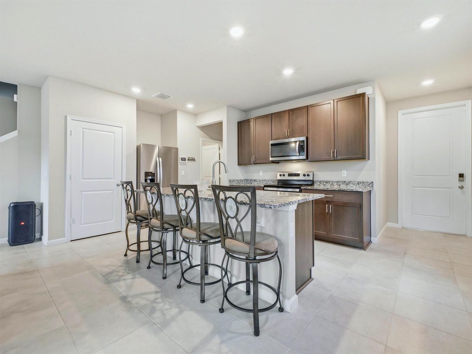 A kitchen features dark wood cabinets, granite countertops, a center island, and four bar stools — 5720 Mentmore Drive, West Palm Beach FL 33407, WEST PALM BEACH, FL
