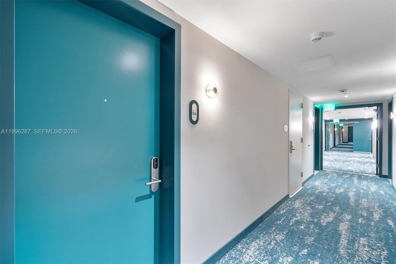 A hallway features a teal door, light-colored walls, and patterned blue carpeting — 77 SE 5th Street # 3004, Miami FL 33131, MIAMI, FL