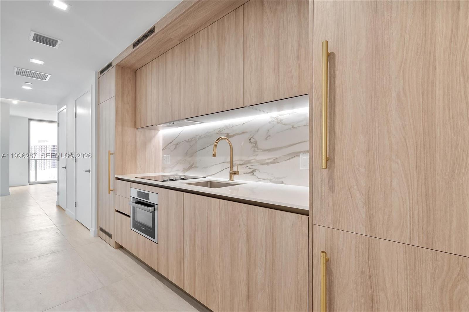 A modern kitchen features light wood cabinetry, gold hardware, and a marble-patterned backsplash — 77 SE 5th Street # 3004, Miami FL 33131, MIAMI, FL
