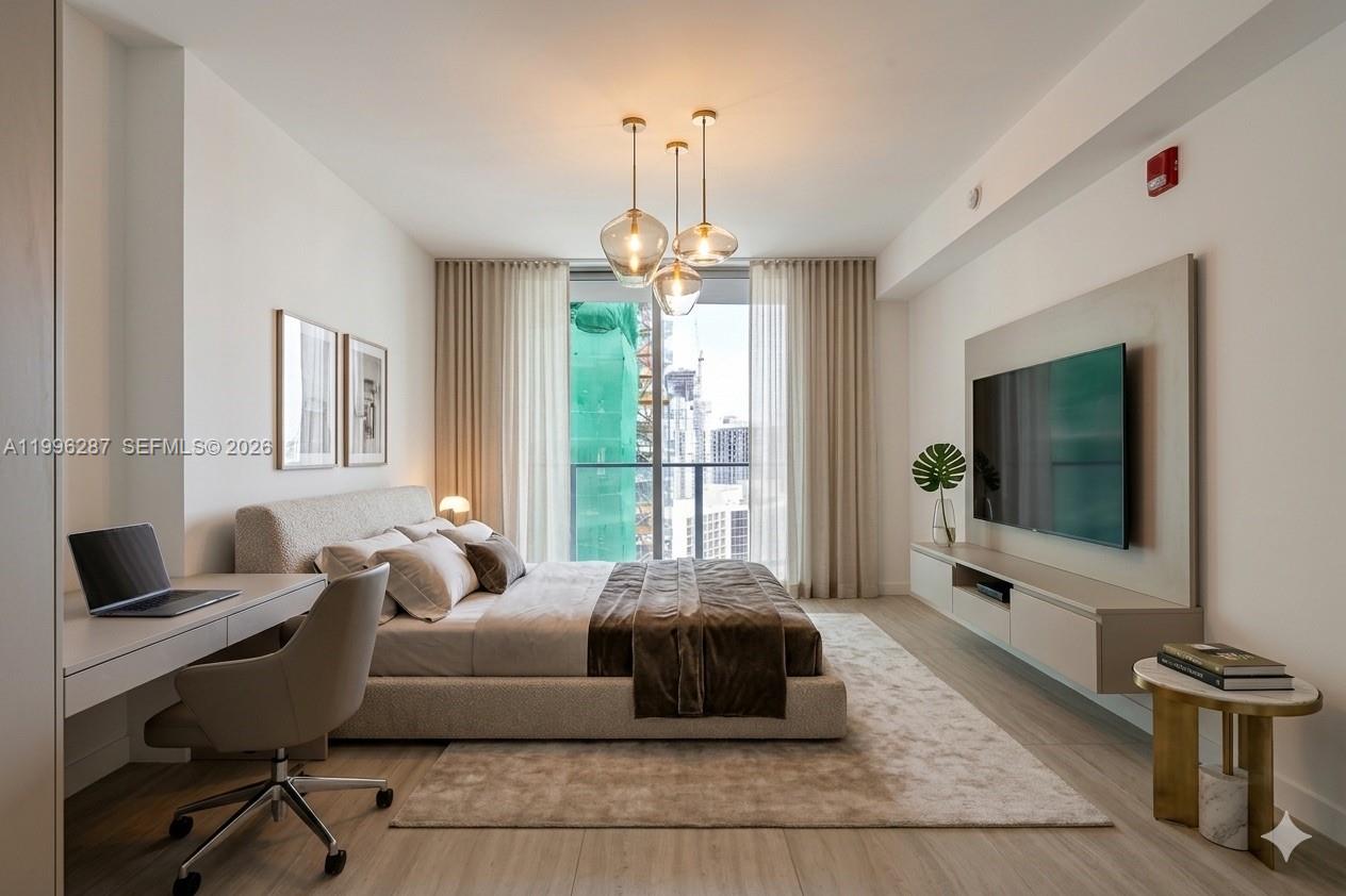 A modern bedroom features a bed, desk, wall-mounted television, and floor-to-ceiling windows with city views — 77 SE 5th Street # 3004, Miami FL 33131, MIAMI, FL