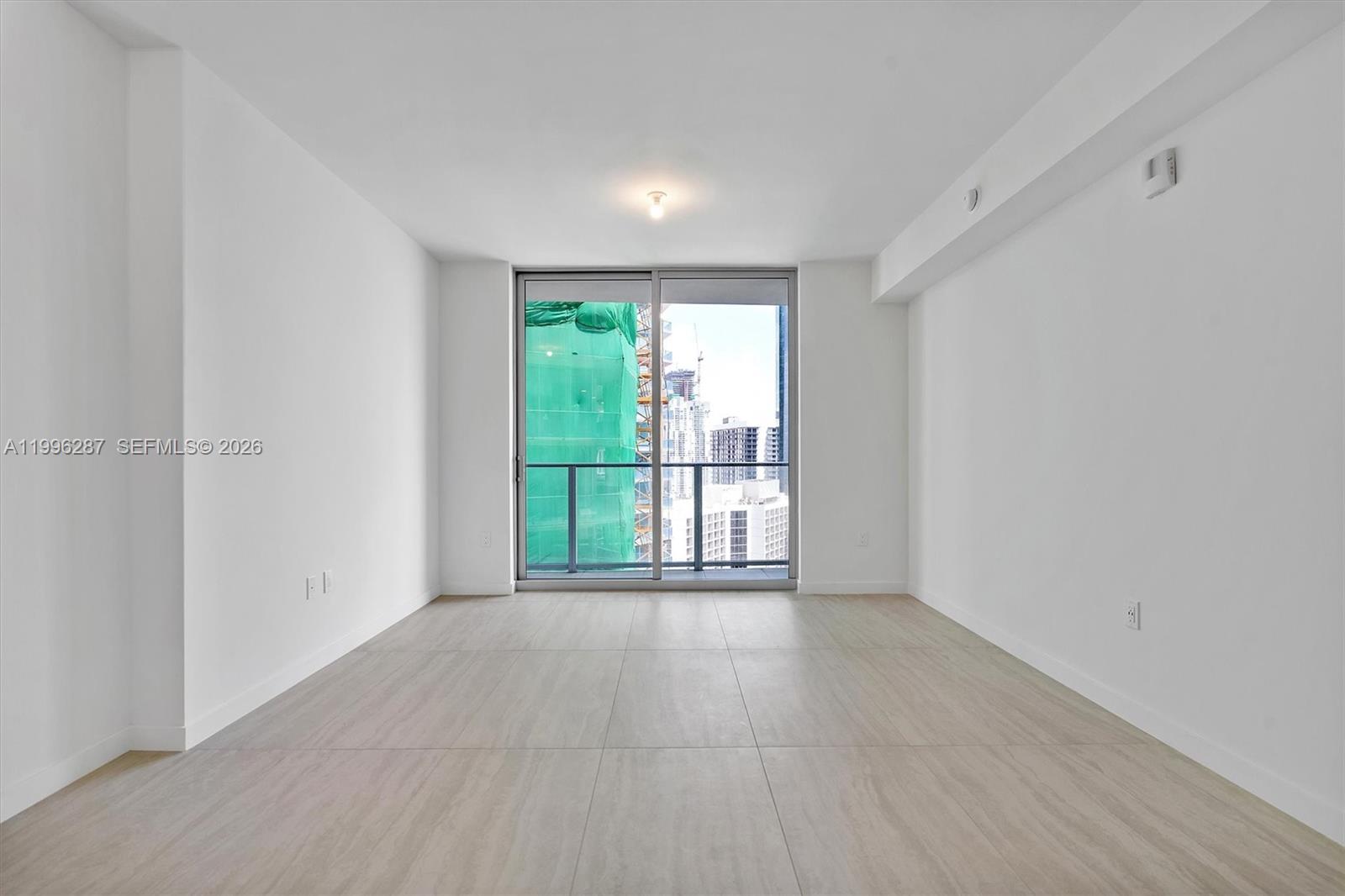 An empty room with white walls, light-colored tile flooring, and a sliding glass balcony door — 77 SE 5th Street # 3004, Miami FL 33131, MIAMI, FL