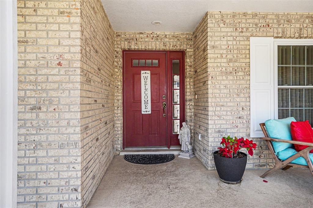 A red front door with a welcome sign sits on a brick-walled porch — 113 SHADDOCK DRIVE, AUBURNDALE, FL