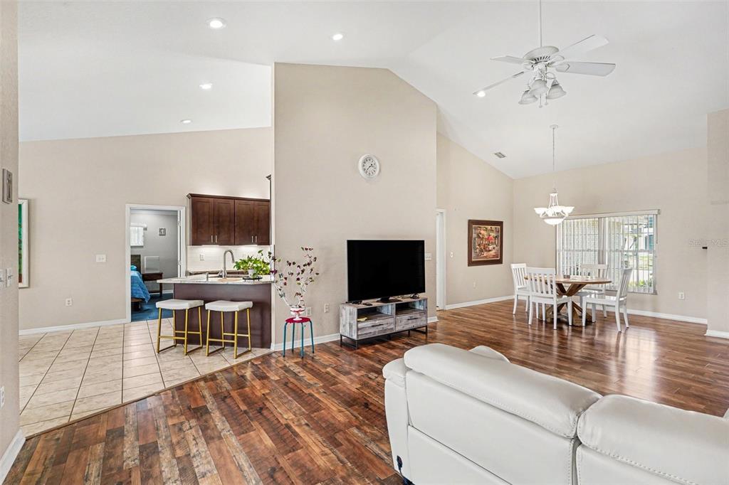 An open-concept living and dining area features wood flooring, a kitchen island, and vaulted ceilings — 113 SHADDOCK DRIVE, AUBURNDALE, FL