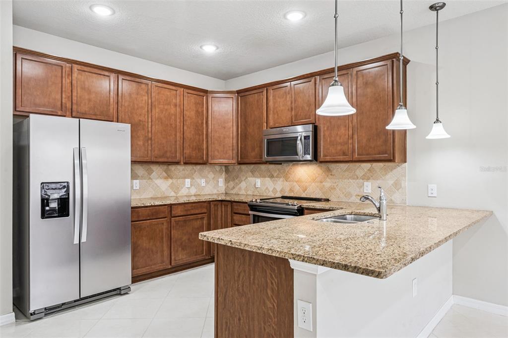A kitchen features brown wooden cabinets, granite countertops, stainless steel appliances, and a breakfast bar — 7260 DUXBURY LN, WINTER GARDEN, FL