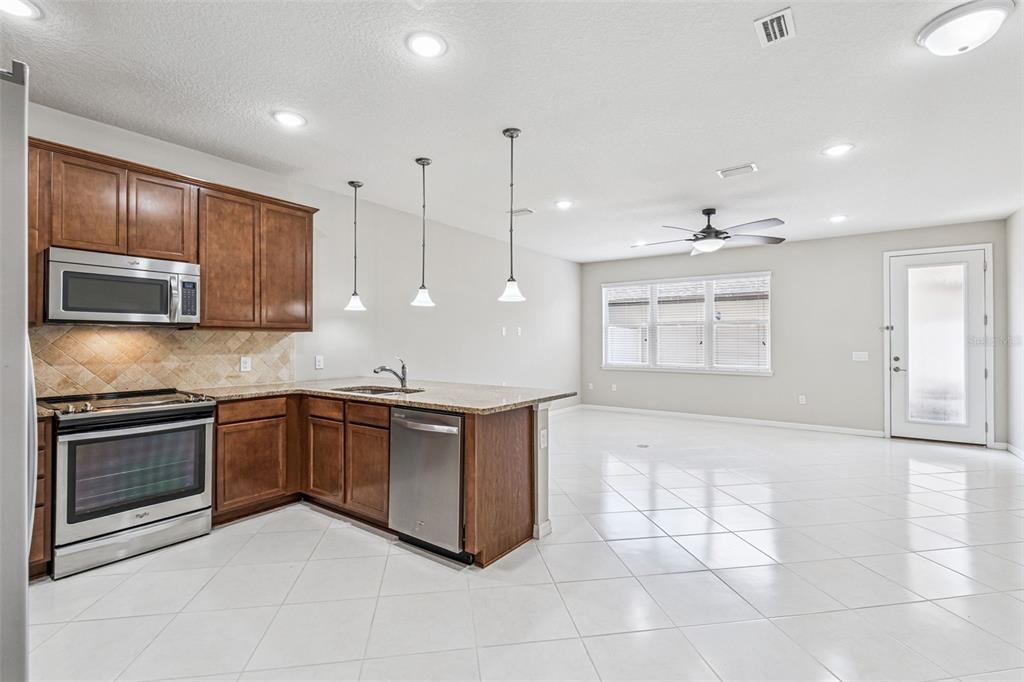 A kitchen with wood cabinets, stainless steel appliances, and an island opens to a living area — 7260 DUXBURY LN, WINTER GARDEN, FL