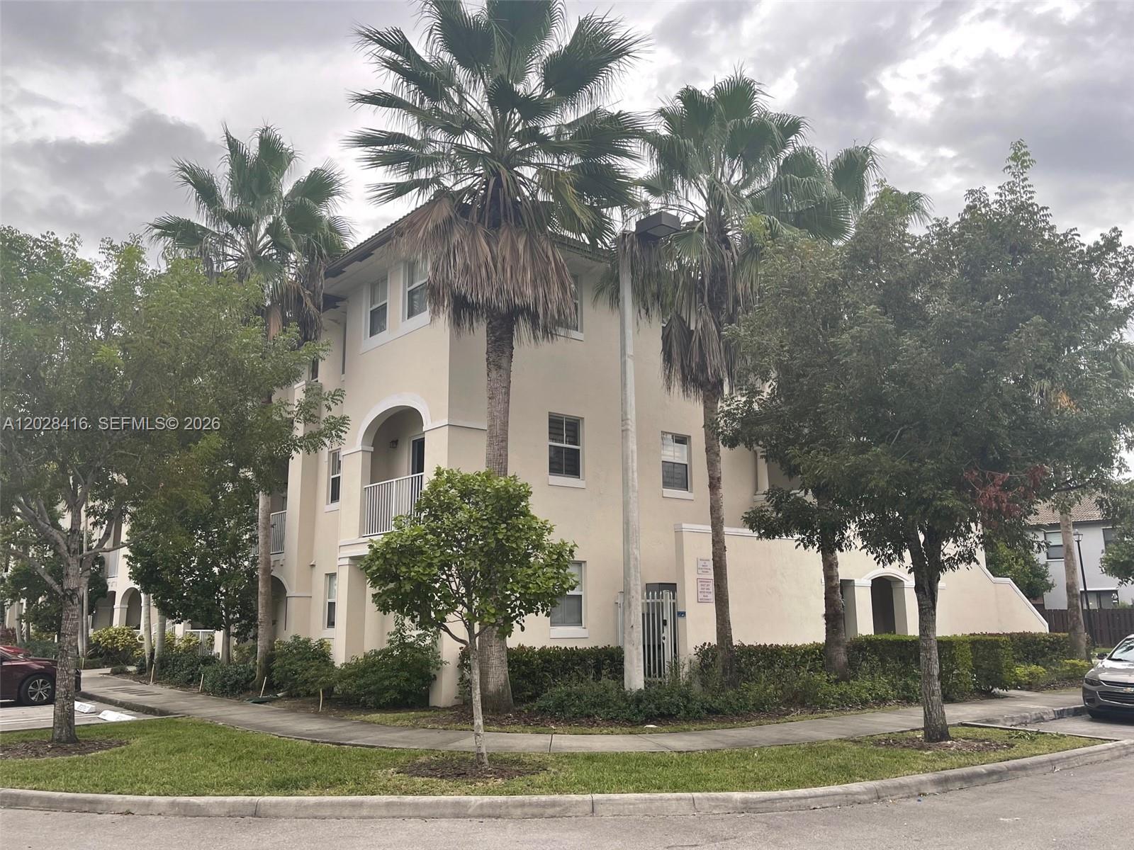 A three-story beige stucco apartment building features palm trees and a sidewalk in front — 11601 NW 89th St # 225, Doral FL 33178, DORAL, FL