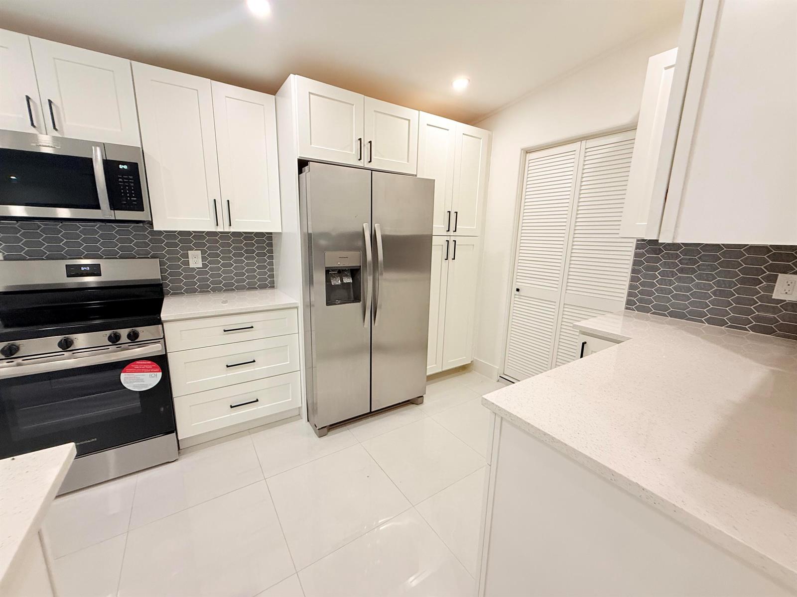 A modern kitchen features white cabinets, stainless steel appliances, quartz countertops, and a gray backsplash — 345 Pinehurst Road, Palm Springs FL 33461, PALM SPRINGS, FL