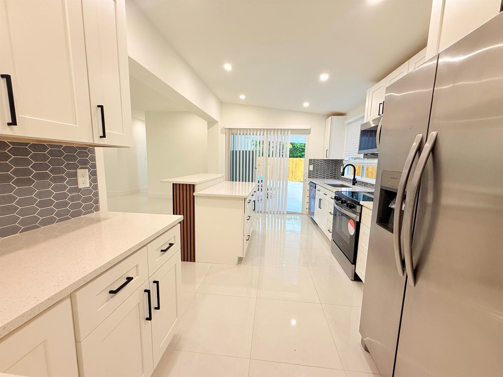 A modern kitchen features white cabinets, stainless steel appliances, quartz countertops, and a gray backsplash — 345 Pinehurst Road, Palm Springs FL 33461, PALM SPRINGS, FL