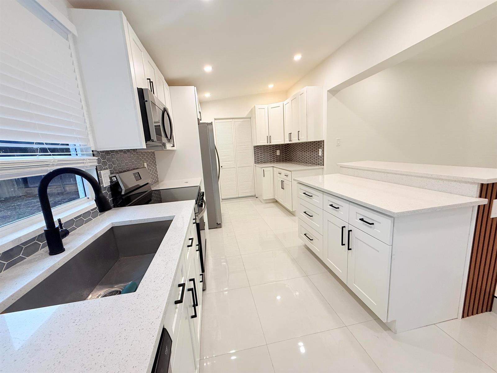 A modern kitchen features white cabinets, quartz countertops, stainless steel appliances, and tiled flooring — 345 Pinehurst Road, Palm Springs FL 33461, PALM SPRINGS, FL