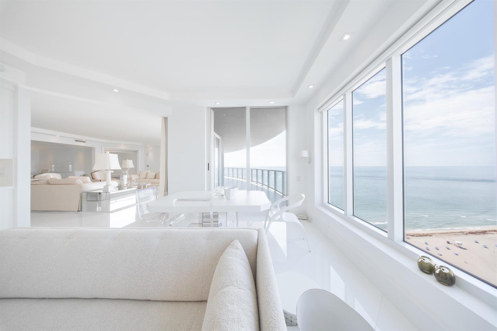 A bright, white living and dining area features floor-to-ceiling windows overlooking the ocean and beach — 2700 N Ocean Drive # 2503a, Riviera Beach FL 33404, RIVIERA BEACH, FL
