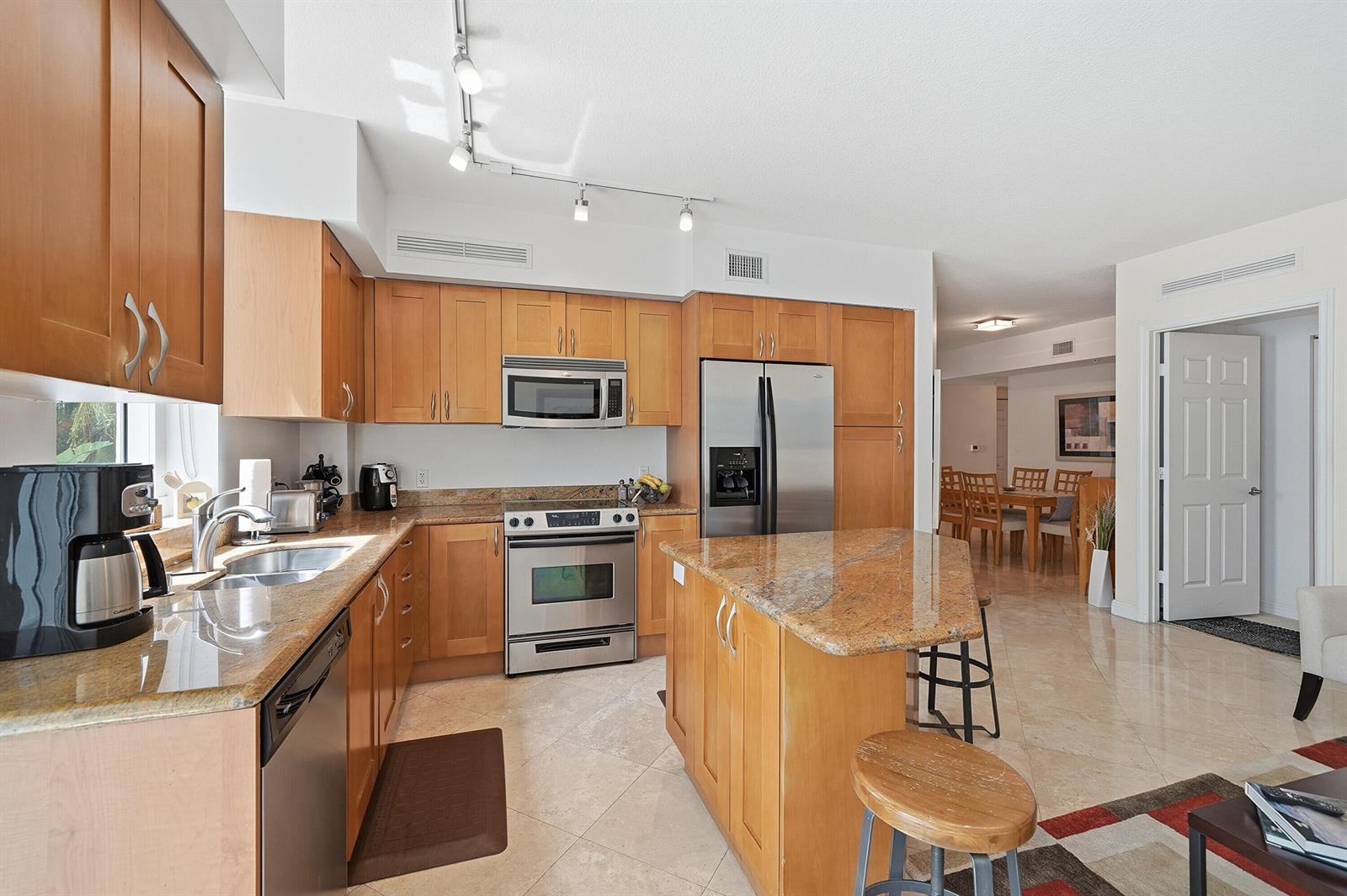 A kitchen with light wood cabinets, granite countertops, stainless steel appliances, and a center island — 1755 E Hallandale Beach Boulevard # 207e, Hallandale Beach FL 33009, HALLANDALE BEACH, FL