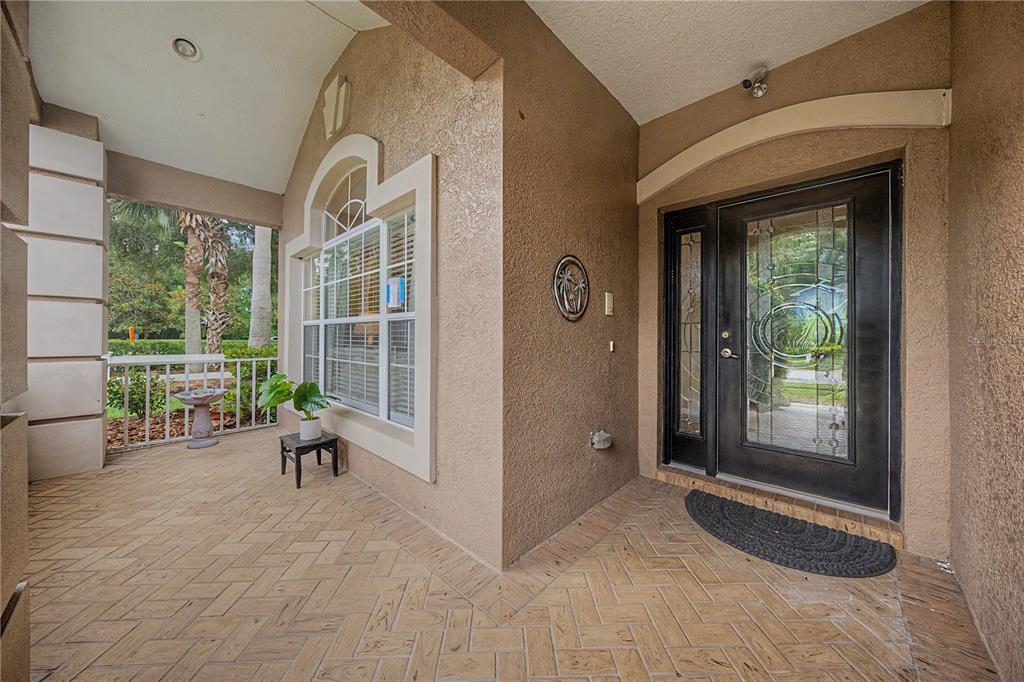 A covered entryway features a herringbone-patterned brick floor, a glass-paneled front door, and a window — 8711 PRESTON WOODS COURT, LAND O LAKES, FL
