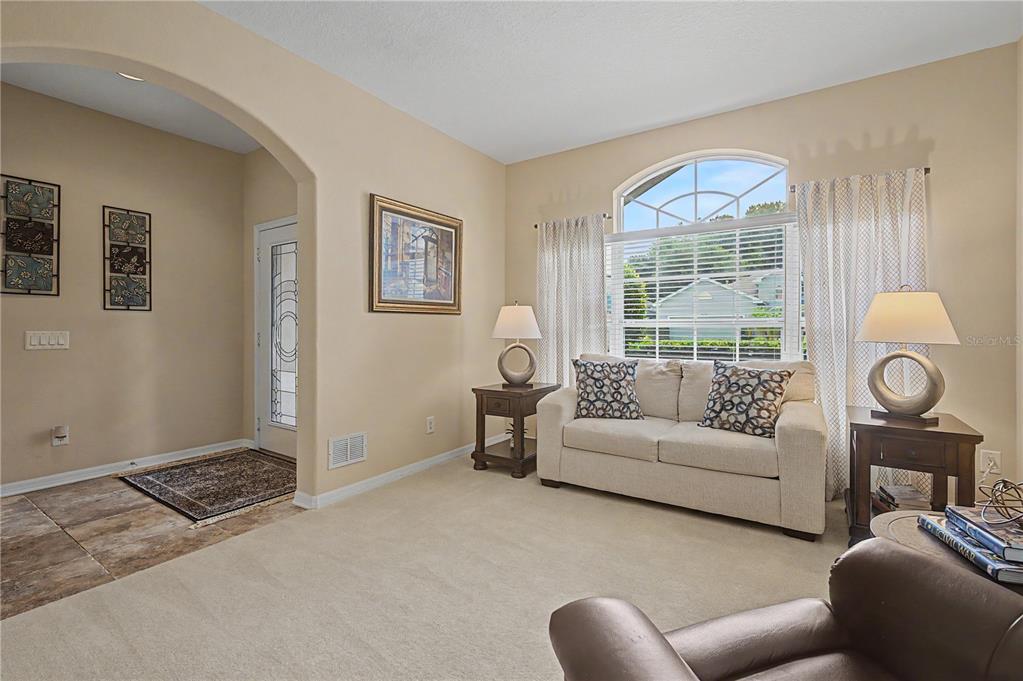 A living room with beige carpet, a light-colored sofa, two side tables, and an arched entryway — 8711 PRESTON WOODS COURT, LAND O LAKES, FL