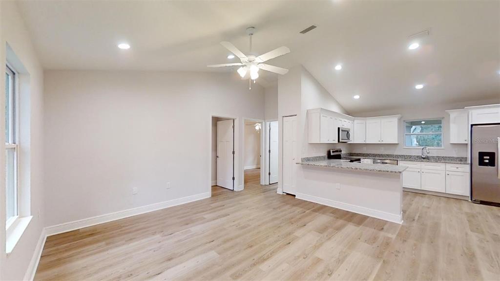 An open-concept kitchen and living area feature white cabinets, light wood flooring, and vaulted ceilings — 24294 NW TAMARIND LANE, DUNNELLON, FL