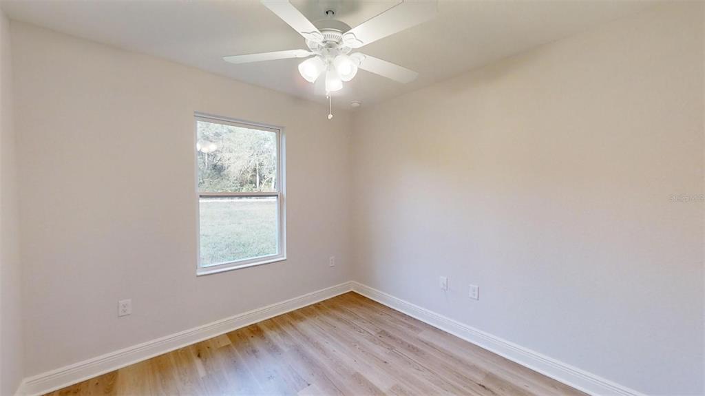 A bedroom with light-colored walls, wood-look flooring, a ceiling fan, and a single window — 24294 NW TAMARIND LANE, DUNNELLON, FL