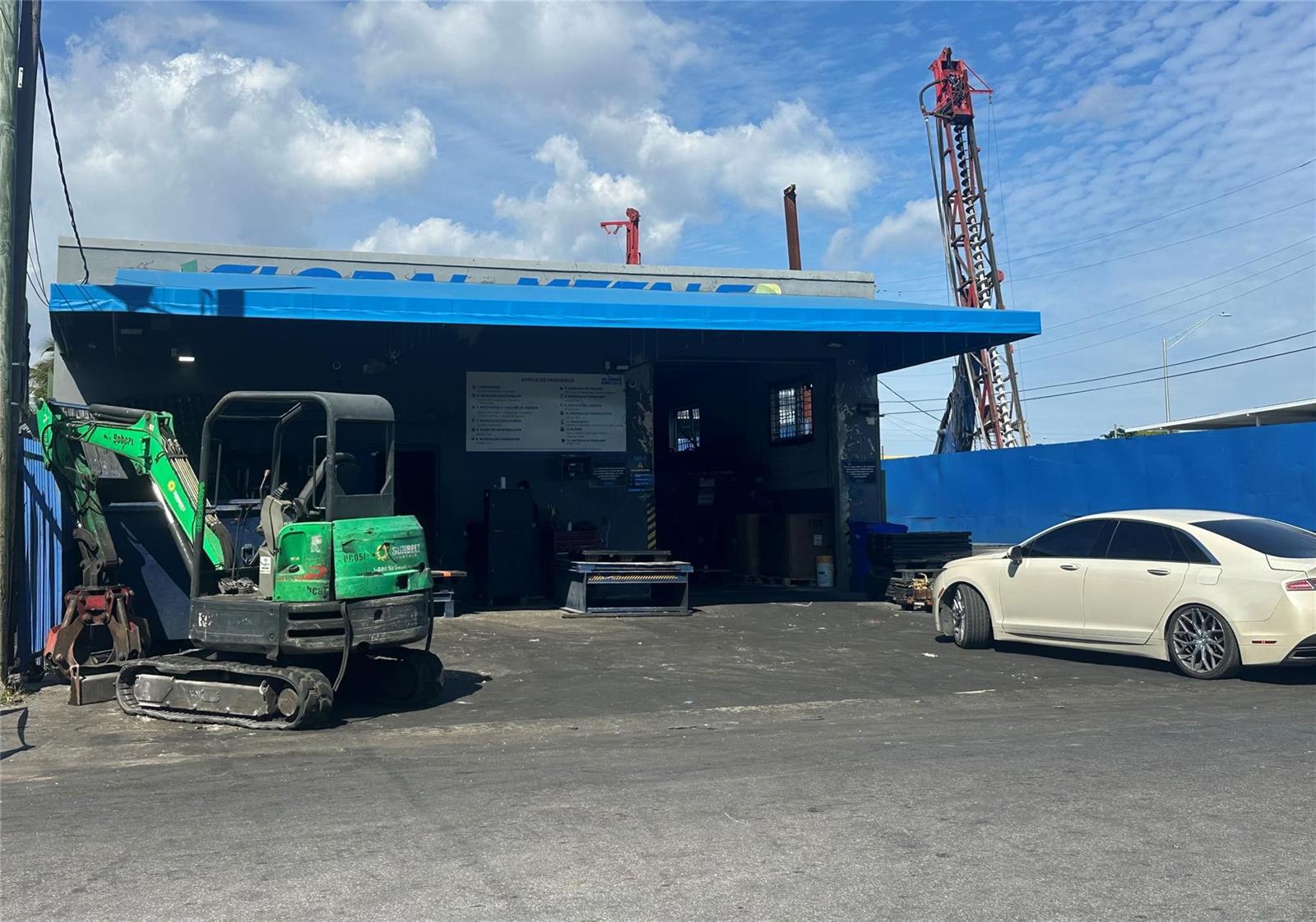 A commercial building with a blue awning, a green excavator, and a white sedan parked outside — 2717 NW 34th Street, Miami FL 33142, MIAMI, FL