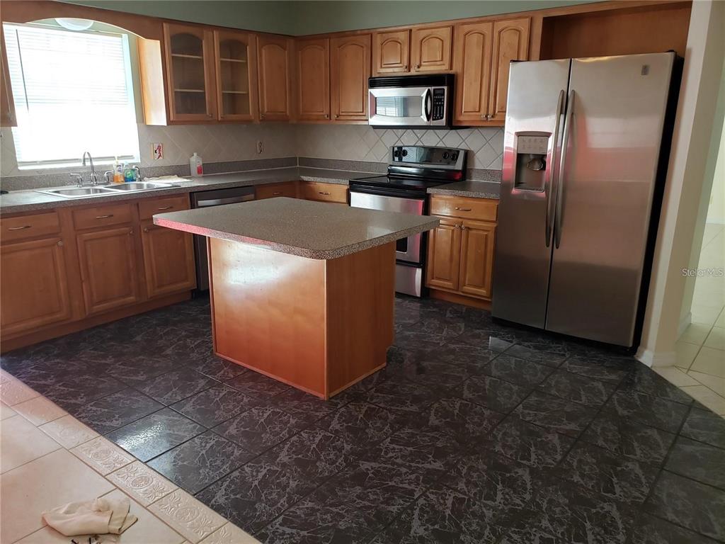 A kitchen features wood cabinets, stainless steel appliances, a central island, and dark tiled flooring — 3792 DUNWICH AVENUE, ORLANDO, FL