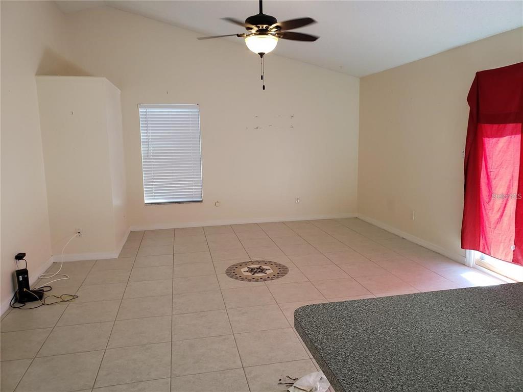 An empty room features light-colored tile flooring, a vaulted ceiling with a fan, and a window — 3792 DUNWICH AVENUE, ORLANDO, FL