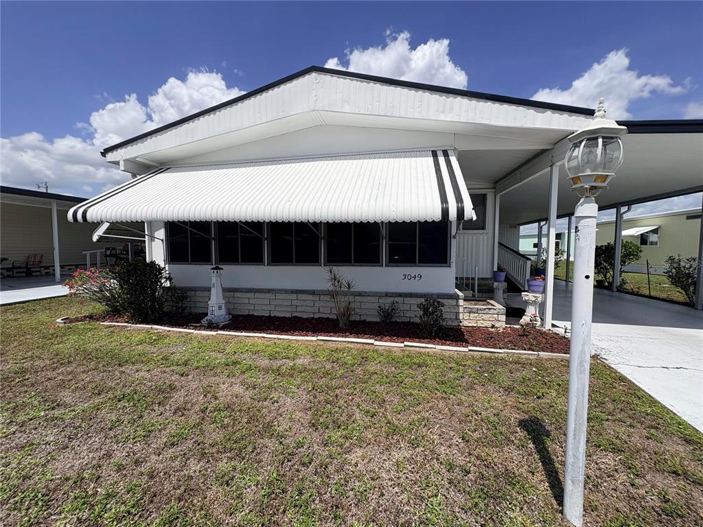 A single-story manufactured home with a white metal awning, carport, and a small lighthouse statue — 3049 LONGVIEW LANE, NORTH FORT MYERS, FL