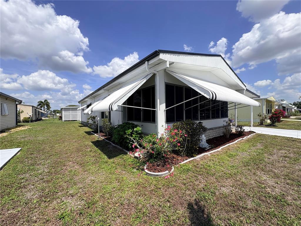 A single-story manufactured home features a screened-in porch with striped metal awnings and landscaping — 3049 LONGVIEW LANE, NORTH FORT MYERS, FL