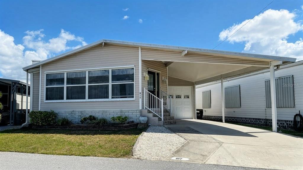 A single-story manufactured home with light siding, a front carport, and a small landscaped garden — 817 S WATERWAY, VENICE, FL