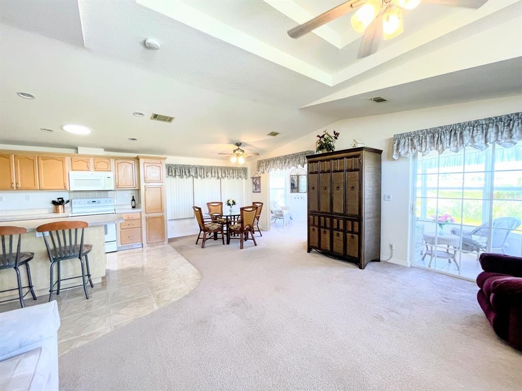 A kitchen with light wood cabinets opens into a carpeted dining and living area — 817 S WATERWAY, VENICE, FL