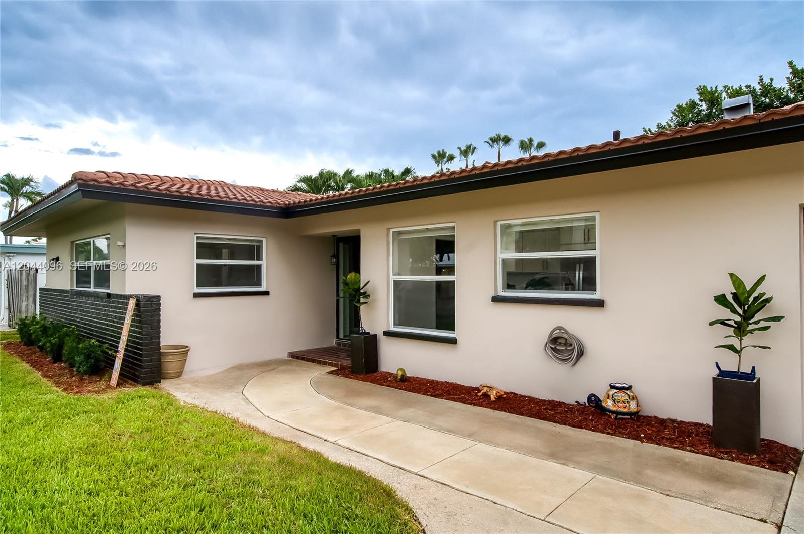 The exterior of a single-story house features a concrete walkway, tiled roof, and landscaping — 106 E Park Ln E, Hypoluxo FL 33462, HYPOLUXO, FL