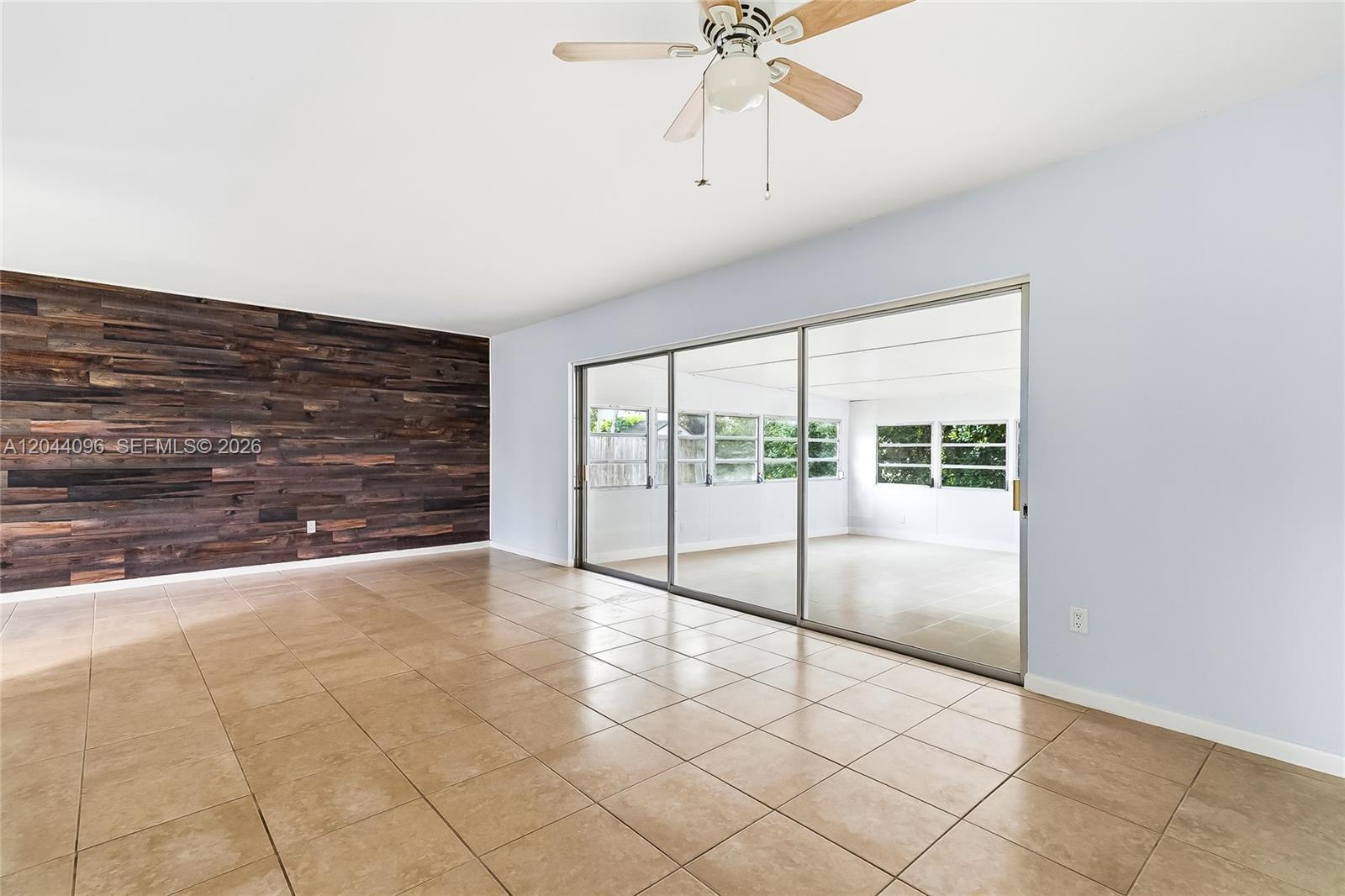 A living room features a wood-plank accent wall, tile flooring, and sliding glass doors — 106 E Park Ln E, Hypoluxo FL 33462, HYPOLUXO, FL