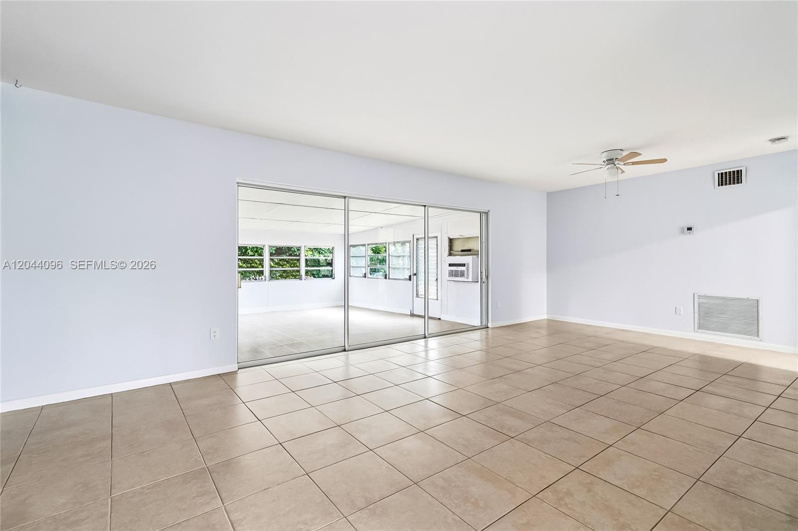 A spacious living room features light-colored walls, beige tile flooring, and sliding glass doors — 106 E Park Ln E, Hypoluxo FL 33462, HYPOLUXO, FL
